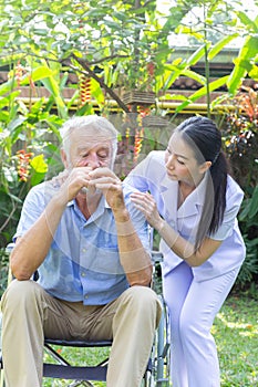 Nurse take care a depressed thoughtful senior retirement man on his wheelchair in a garden in his home