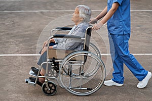 nurse take care and pushing senior woman in wheelchair at park, friendly caregiver