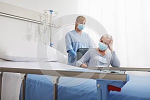 Nurse take comfort elderly woman in wheelchair wearing surgical protective medical masks in hospital room, concept of isolation