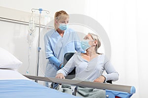 Nurse take comfort elderly woman in wheelchair wearing surgical protective medical masks in hospital room, concept of isolation