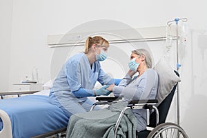 Nurse take comfort elderly woman in wheelchair wearing surgical protective medical masks in hospital room, concept of isolation