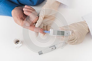 A nurse takes a blood sample with an old man`s scarifier. The nurse takes the blood to the glycemeter.