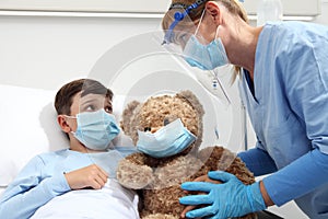 Nurse takes care of the patient child in hospital bed playing with teddy bear, wearing protective masks, corona virus covid 19