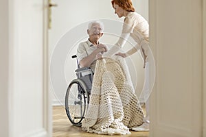 Nurse taking care of happy elderly man in a wheelchair in his ho