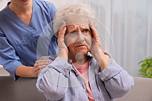 Nurse taking care of senior woman with headache indoors