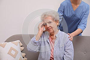 Nurse taking care of senior woman with headache indoors
