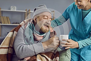 Nurse taking care of a sick retired senior man, helping him and making him hot tea