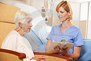 Nurse Taking Notes From Senior Female Patient Seated In Chair