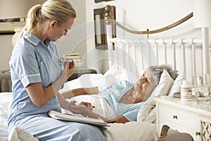 Nurse Taking Pulse Of Senior Patient Patient In Bed At Home