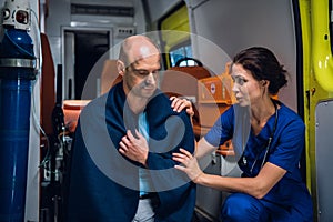 Nurse talking friendly with a patient sitting in a blanket in an ambulance car