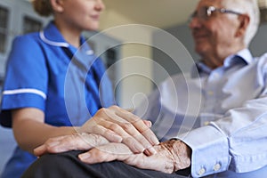 Nurse Talking With Senior Man Sitting In Chair On Home Visit