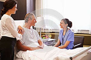 Nurse Talking To Male Patient And Wife In Hospital Bed