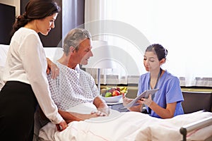 Nurse Talking To Male Patient And Wife In Hospital Bed