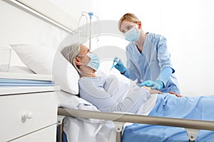 Nurse with thermometer measures fever on elderly woman patient lying in the hospital room bed, wearing protective gloves and