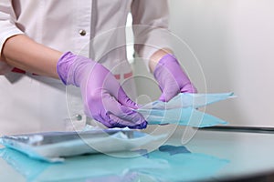 A nurse in a uniform and medical mask lays out sterile dental instruments Packed in a Kraft bag. Photo without a face. Gloved hand
