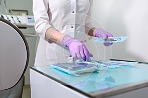 A nurse in a uniform and medical mask lays out sterile dental instruments Packed in a Kraft bag. Unrecognizable photo.Gloved hand