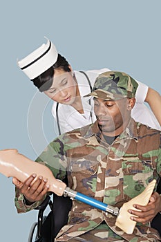 Nurse with US Marine Corps soldier holding artificial limb as he sits in wheelchair over light blue background
