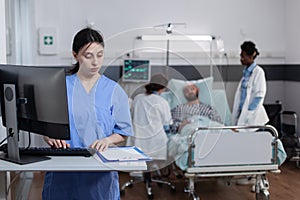 Nurse using personal computer to complete patient admission chart while looking at clipboard with medical history