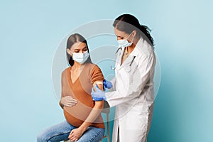 Nurse Vaccinating Pregnant Female Patient Against Covid-19 Over Blue Background