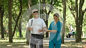 Nurse walking with old blind man along hospice park, property care and support