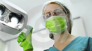 Nurse wearing protection mask glasses and cap adjusting light before examination