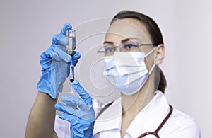A nurse wearing protective gloves and a mask dials a vaccine into a syringe, the concept of vaccinating the population