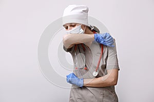 Nurse wearing protective workwear and sneezing into elbow during coronavirus epidemic on white background