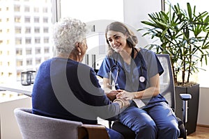 Nurse Wearing Scrubs In Office Reassuring Senior Female Patient And Holding Her Hands