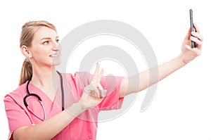 Nurse wearing scrubs taking selfie with smartphone showing peace