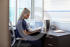 Nurse Wearing Scrubs Working At Desk In Office