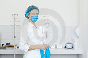 A nurse in a white coat puts on gloves before a medical procedure in a bright handling room