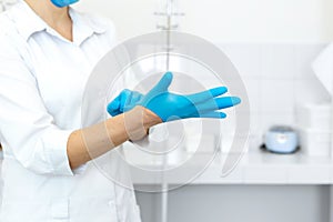 A nurse in a white coat puts on rubber gloves before a medical procedure in a bright handling room