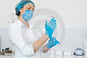 A nurse in a white coat puts on rubber gloves before a medical procedure in a bright handling room photo