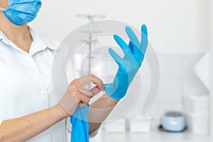 A nurse in a white coat puts on rubber gloves before a medical procedure in a bright handling room
