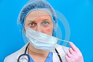 Nurse after work removes the medical mask, close-up. Doctor in a medical gown with a tired face, blue background. Concept stay
