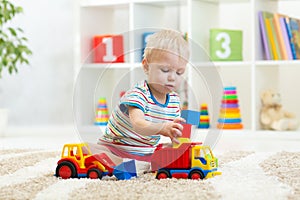 Nursery baby plays block and car toys sitting on carpet indoors