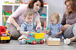 Nursery kids playing with toys. Mothers communicate and watch over their children