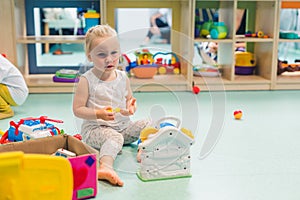 Nursery school. Toddler girl playing with different plastic toys such as building blocks, car toys, playhouses. Work on