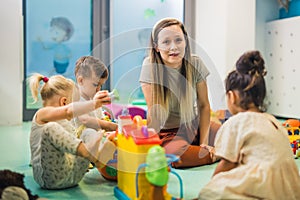 Nursery school. Toddlers and their teacher playing with colorful plastic playhouses, cars and boats. Imagination