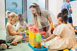 Nursery school. Toddlers and their teacher playing with colorful plastic playhouses, cars and boats. Imagination