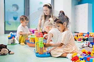 Nursery school. Toddlers and their teacher playing with colorful plastic playhouses, cars and boats. Imagination