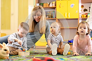 Nursery teacher looking after children in daycare. Little kids toddlers play together with developmental toys.