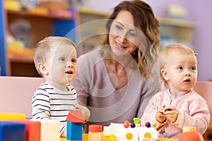 Nursery teacher looking after children in daycare. Little kids toddlers play together with developmental toys
