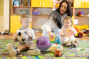 Nursery teacher looking after children in daycare. Little kids toddlers play together with developmental toys