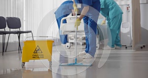 Nurses mopping floor and making bed in empty hospital ward