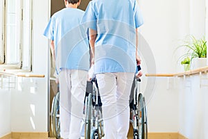 Nurses pushing seniors in wheelchair thru nursing home