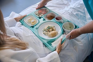 Nursing assistant serving meal to recumbent patient