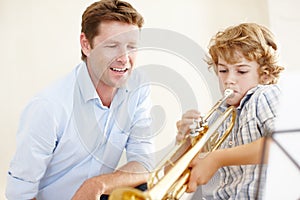 Nurturing his musical talent. a cute little boy playing the trumpet while his father watches him proudly.