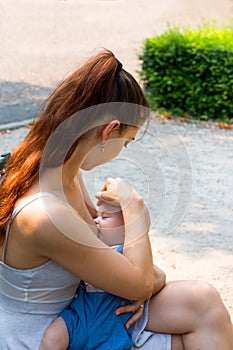 Nurturing mother breastfeeding innocent baby close up, sitting outdoor