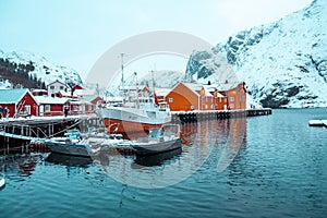 Nusfjord, small fishing village in Norway, during amazing winter evening, ships, snow and yellow cabins.